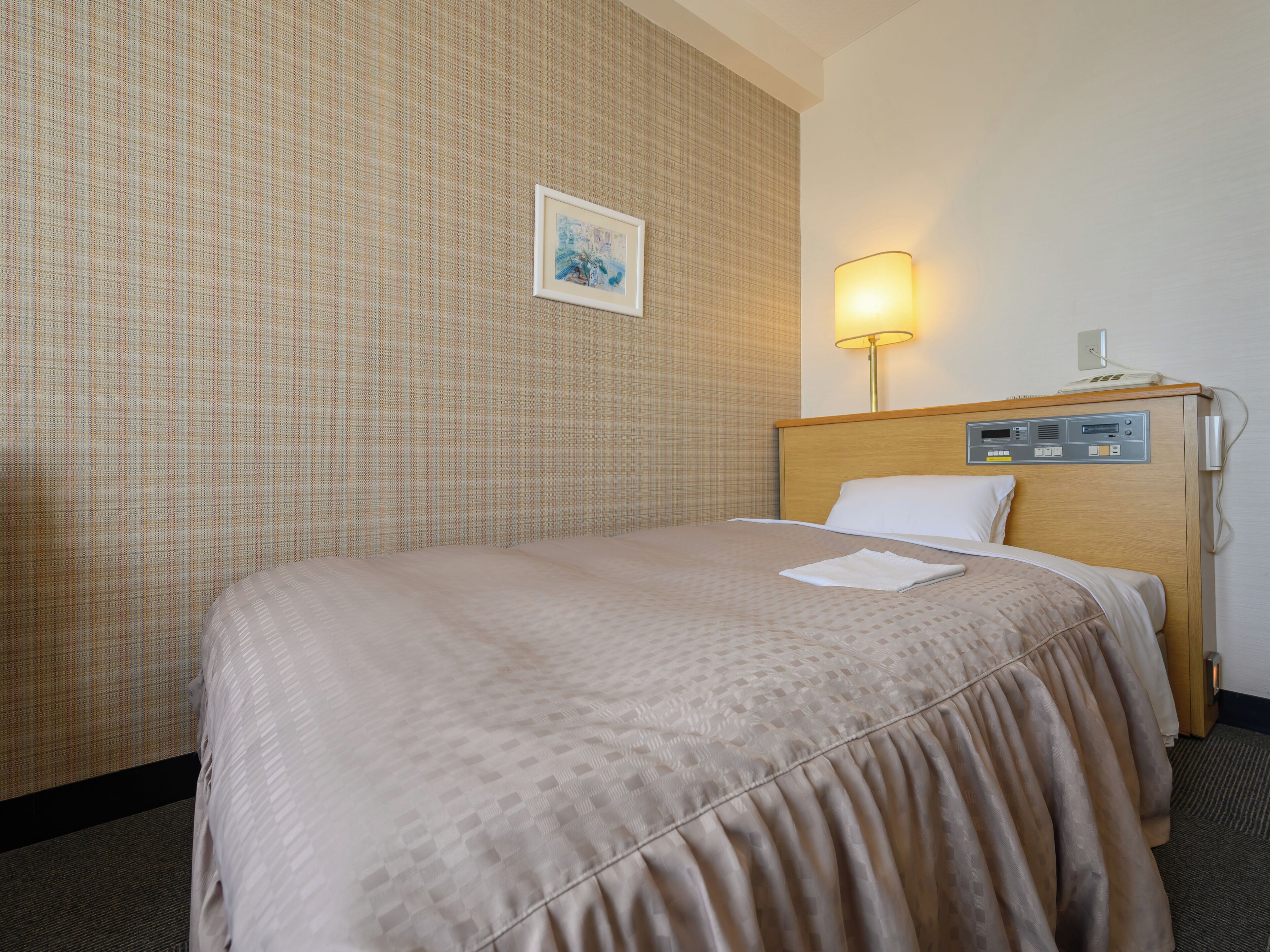 Una habitación de hotel con una cama, una lámpara de noche, un panel de control y un cuadro en la pared.