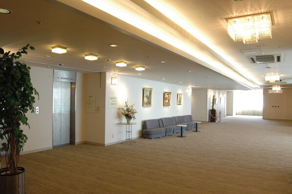 A spacious lobby with a wooden floor, a reception desk, a sofa, and a chandelier.