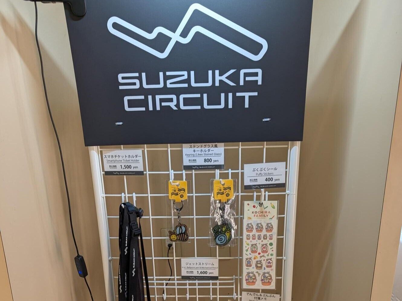 A wall with a 'Suzuka Circuit' sign and various items for sale including keychains and stickers.