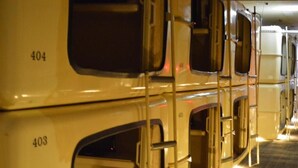 A train carriage interior with numbered compartments, metal handrails, and a carpeted floor. - ATSUGI CAPSULEHOTEL – Caters to Men (Atsugi)