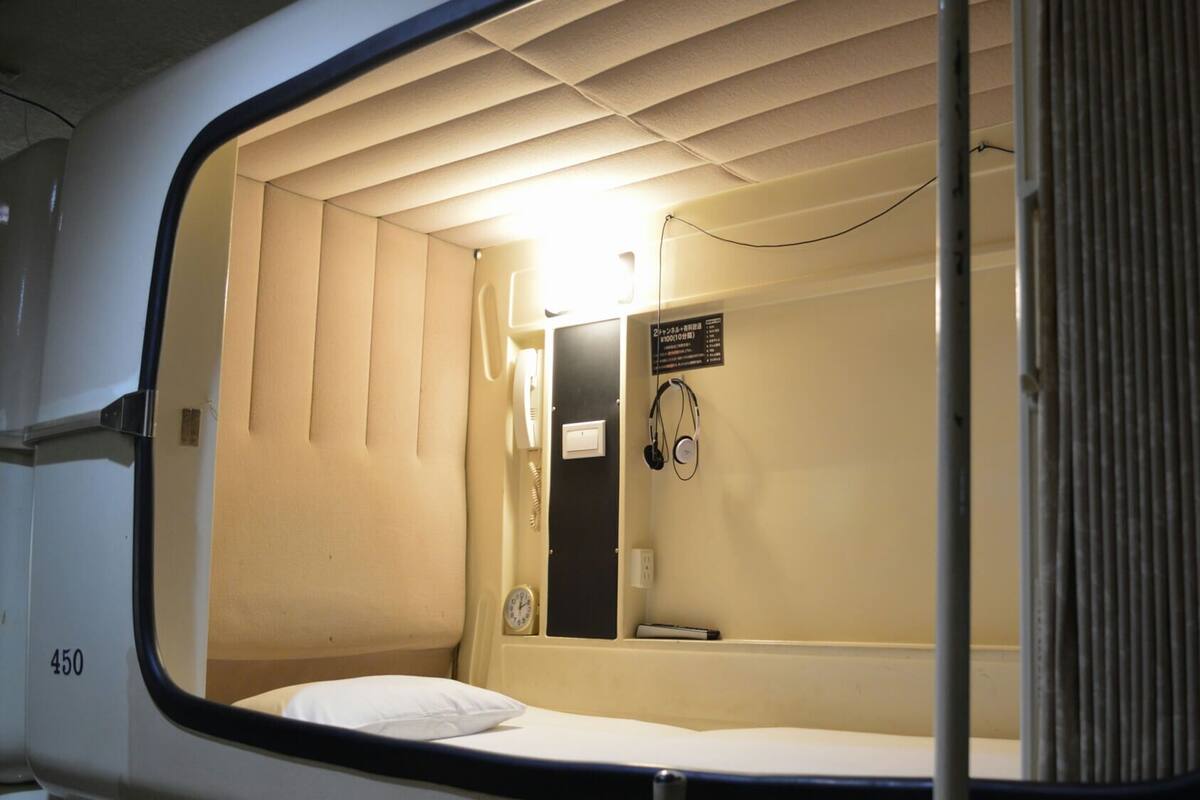 Un espacio pequeño y cerrado con una cama individual, un reloj en la pared y un letrero con texto en japonés.