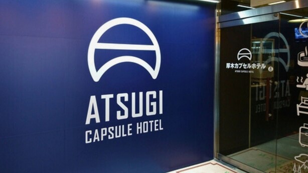 A blue wall with the ATSUGI CAPSULE HOTEL logo and Japanese text. - ATSUGI CAPSULEHOTEL – Caters to Men (Atsugi)