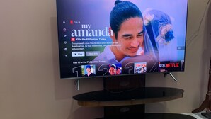 A television on a wooden stand with a remote control on the floor. - Mactan Transient Townhouse (Lapu-Lapu)