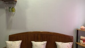 A bedroom with a wooden headboard, three patterned pillows, a shelf with decorative items, and a wall-mounted wine rack with glasses. - Mactan Transient Townhouse (Lapu-Lapu)
