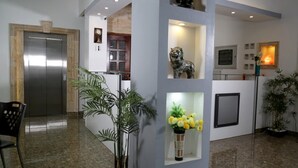 A lobby with a reception desk, a clock, a statue, and a plant. - Fantazia Hotel (Oran)