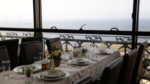 A dining table set for two with a view of the sea through large windows. - Fantazia Hotel (Oran)
