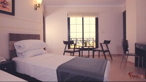 A hotel room with a bed, bedside table with a phone, a desk with a chair, and a window with a view of a balcony. - Fantazia Hotel (Oran)
