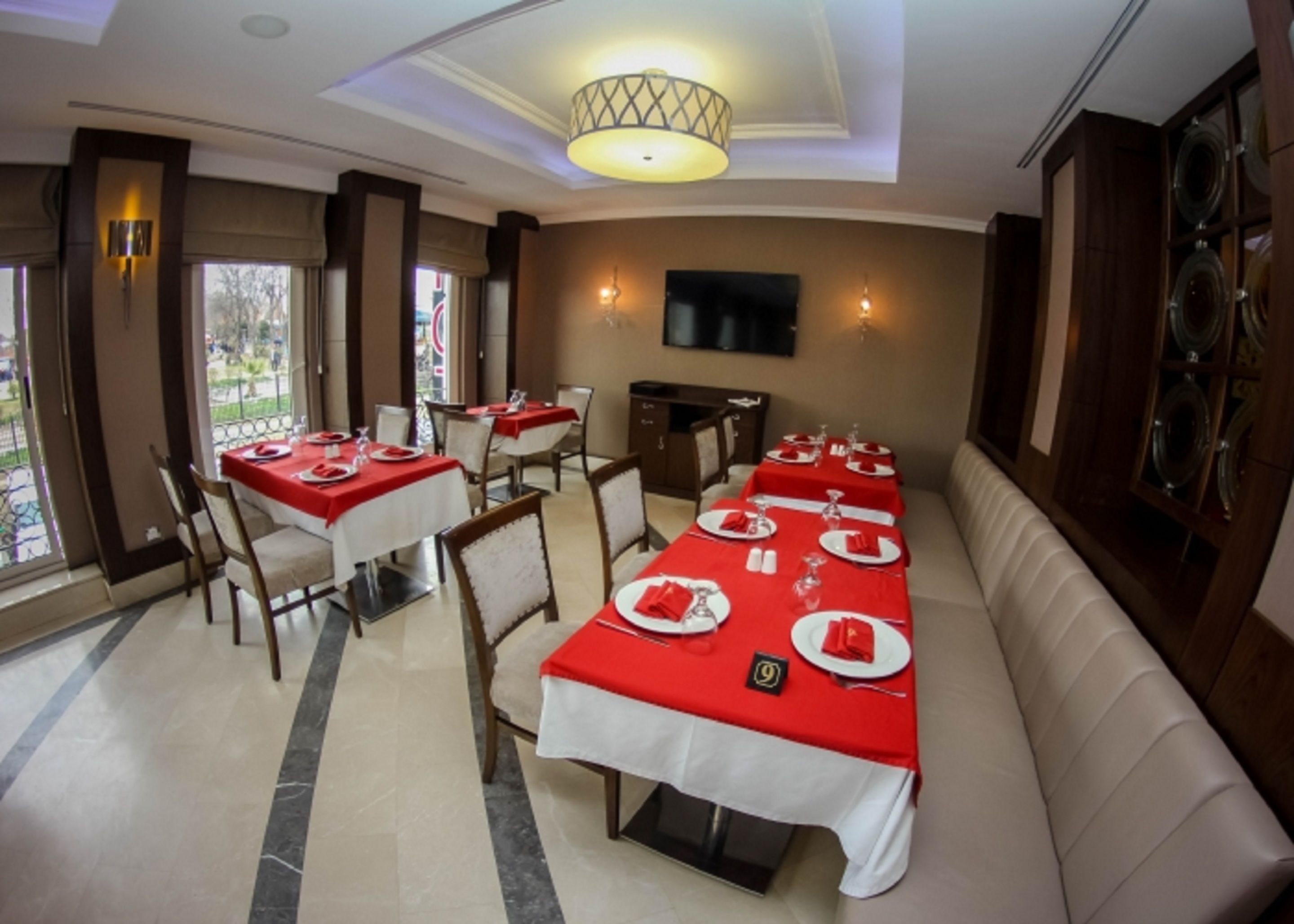 A dining area with tables set for a meal, a sofa, and a television on the wall.