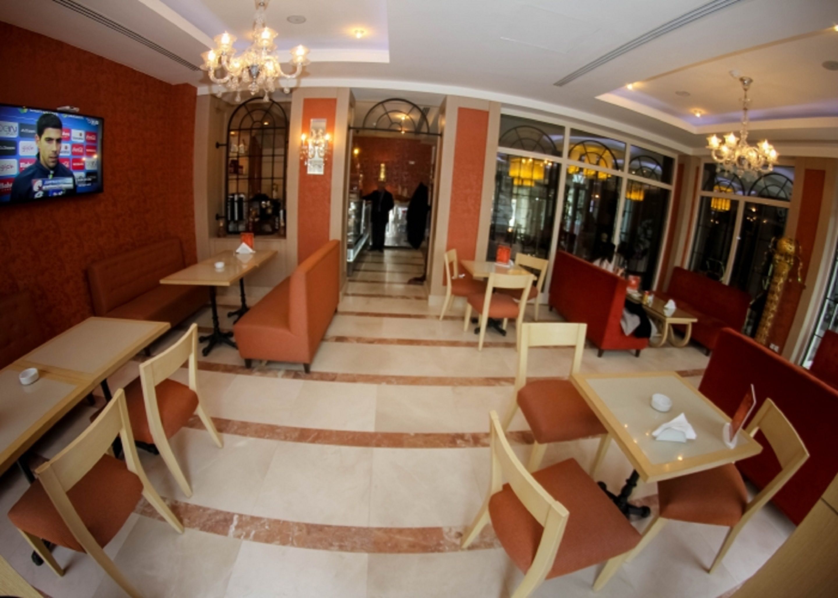A restaurant with booths and tables, a TV on the wall, and a chandelier.