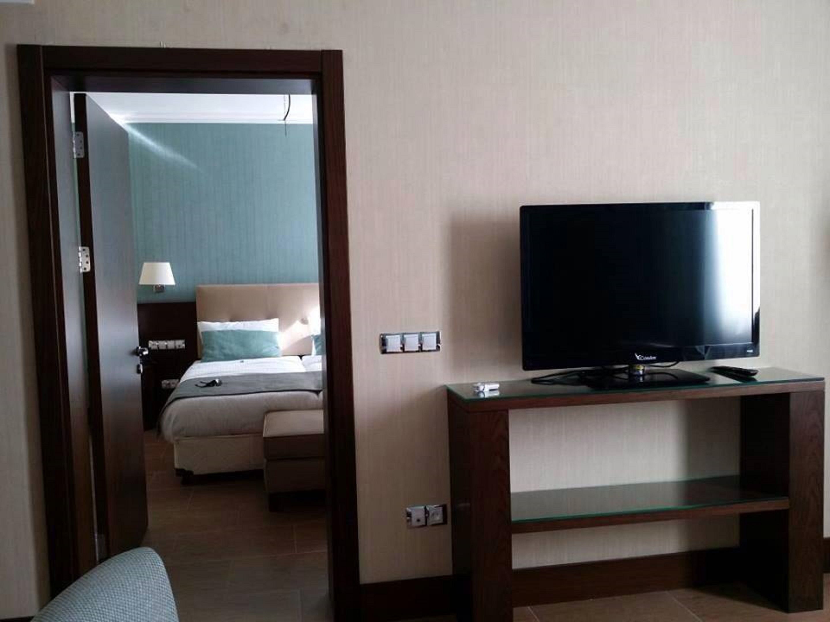 Een hotelkamer met een bed, een televisie op een standaard en een deur naar een andere kamer.