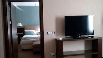 Een hotelkamer met een bed, een televisie op een standaard en een deur naar een andere kamer.