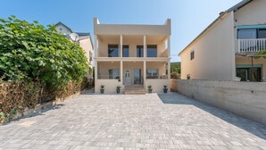 Un bâtiment moderne à deux étages, doté d’une entrée centrale, de plantes en pot et d’une cour dallée.