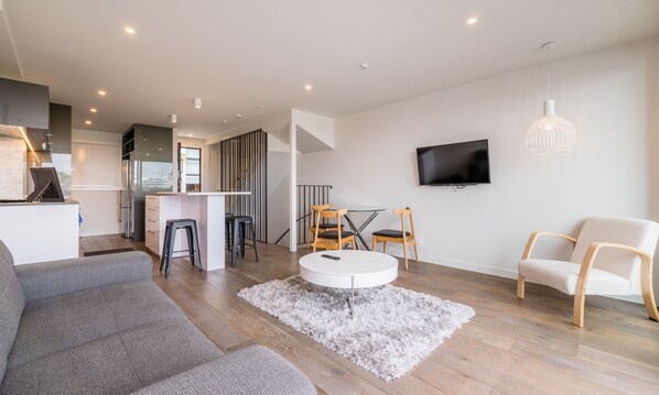 A modern living room with a grey sofa, a white coffee table, and a TV mounted on the wall.