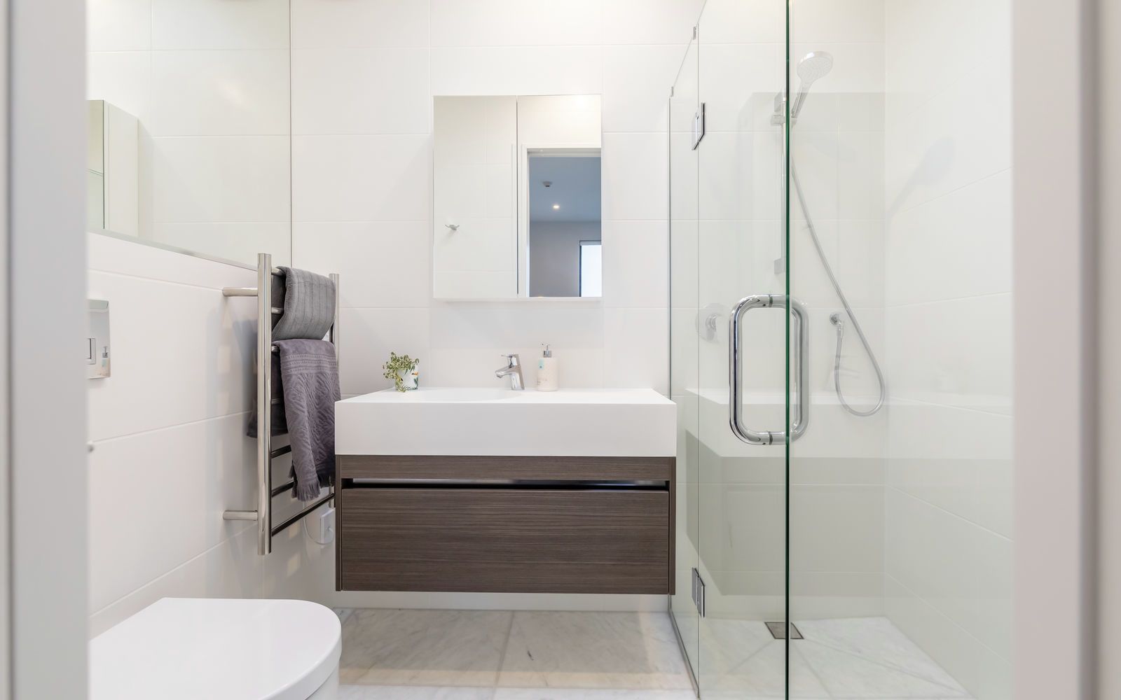 A modern bathroom with a white sink, dark wood vanity, a glass shower enclosure, and a toilet.