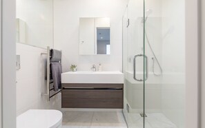 A modern bathroom with a white sink, dark wood vanity, a glass shower enclosure, and a toilet.