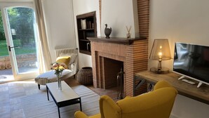 Una sala de estar con chimenea, un sofá, un sillón amarillo, un televisor y una estantería.