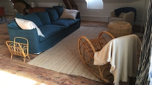 Un dormitorio estilo loft acogedor con un sofá azul, una silla de mimbre y un ventanal grande.