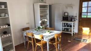 Un comedor con una mesa de mármol, sillas de madera y un armario blanco con cristalería.
