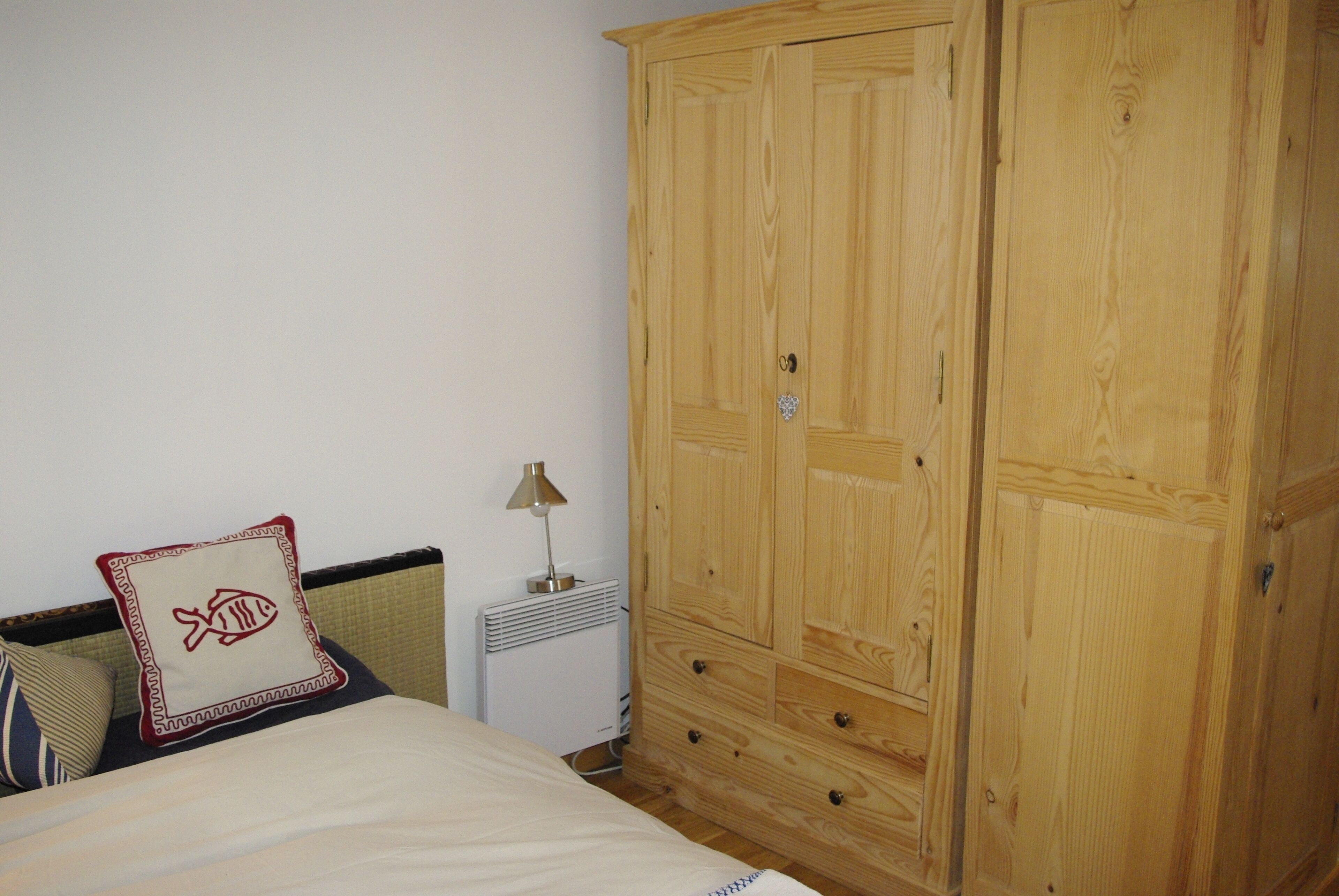 Un dormitorio con una cama, un armario de madera, un radiador y una lámpara.