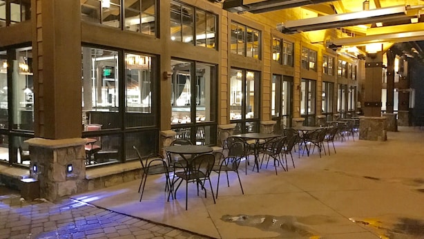 An outdoor seating area with tables and chairs, a stone-paved floor, and large windows with interior lighting. - Five Star Grand Lodge @ Peak 7:  Week of July 4th! (Breckenridge)