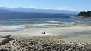 Ein Strand mit klarem Wasser, Bergen im Hintergrund und einigen Spaziergängern.