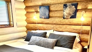 Ein schlafzimmerähnlicher Raum im Stil einer Blockhütte mit einem Bett, Kissen und zwei Wandleuchten.