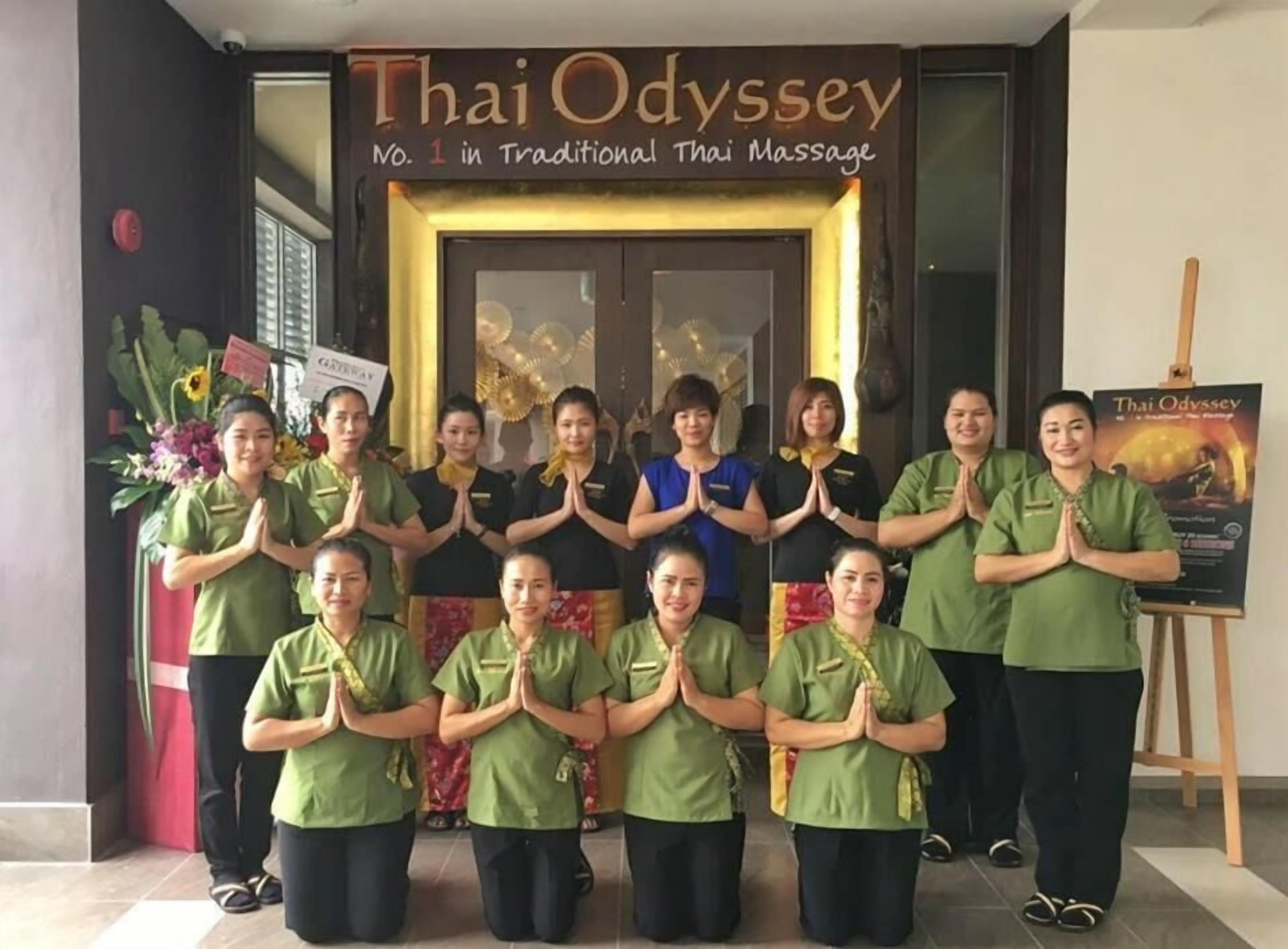 Un grup de persones uniformades de verd al davant d'un centre de massatge tailandès anomenat 'Thai Odyssey'.