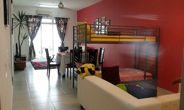 A room with a bunk bed, a dining table with chairs, a sofa, and a potted plant.