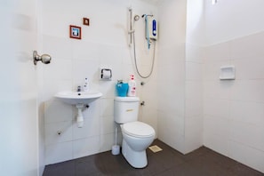 A small, clean bathroom with a white sink, toilet, and shower. There are two small framed pictures on the wall and a soap dispenser on the sink.