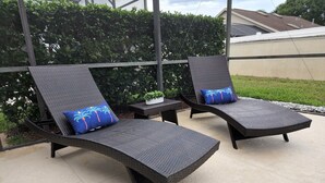 Two dark wicker lounge chairs with blue cushions, positioned on a concrete patio with a hedge and a building in the background. - Family friendly, 10 mins to Disney, WIFI, Resort style amenities, Backyard pool (Kissimmee)