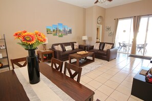 A living room with a sofa set, a dining table, and a vase of sunflowers. - Family friendly, 10 mins to Disney, WIFI, Resort style amenities, Backyard pool (Kissimmee)