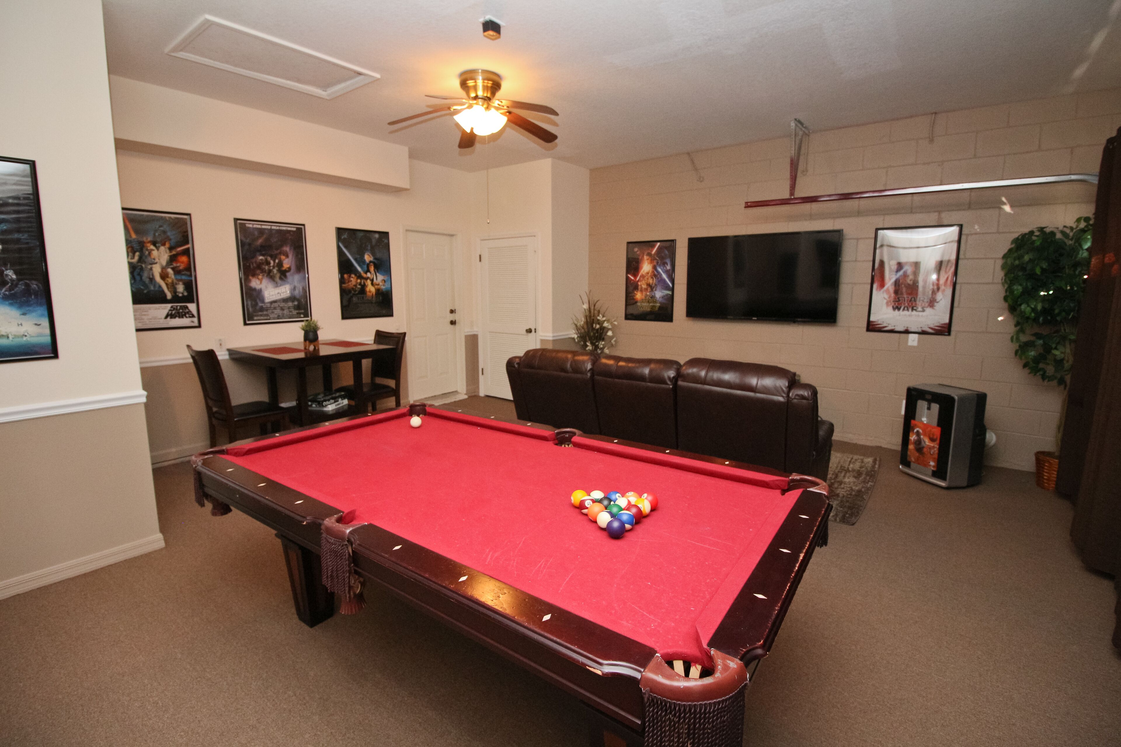 A pool table with balls, a ceiling fan, and wall-mounted televisions.