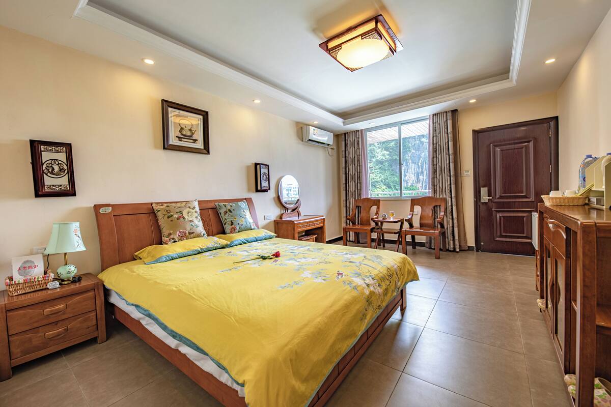 A hotel room with a bed, bedside table, lamp, framed pictures, a desk, chair, and a window with curtains.