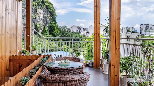 A balcony with wicker furniture, potted plants, and a view of a mountainous area.