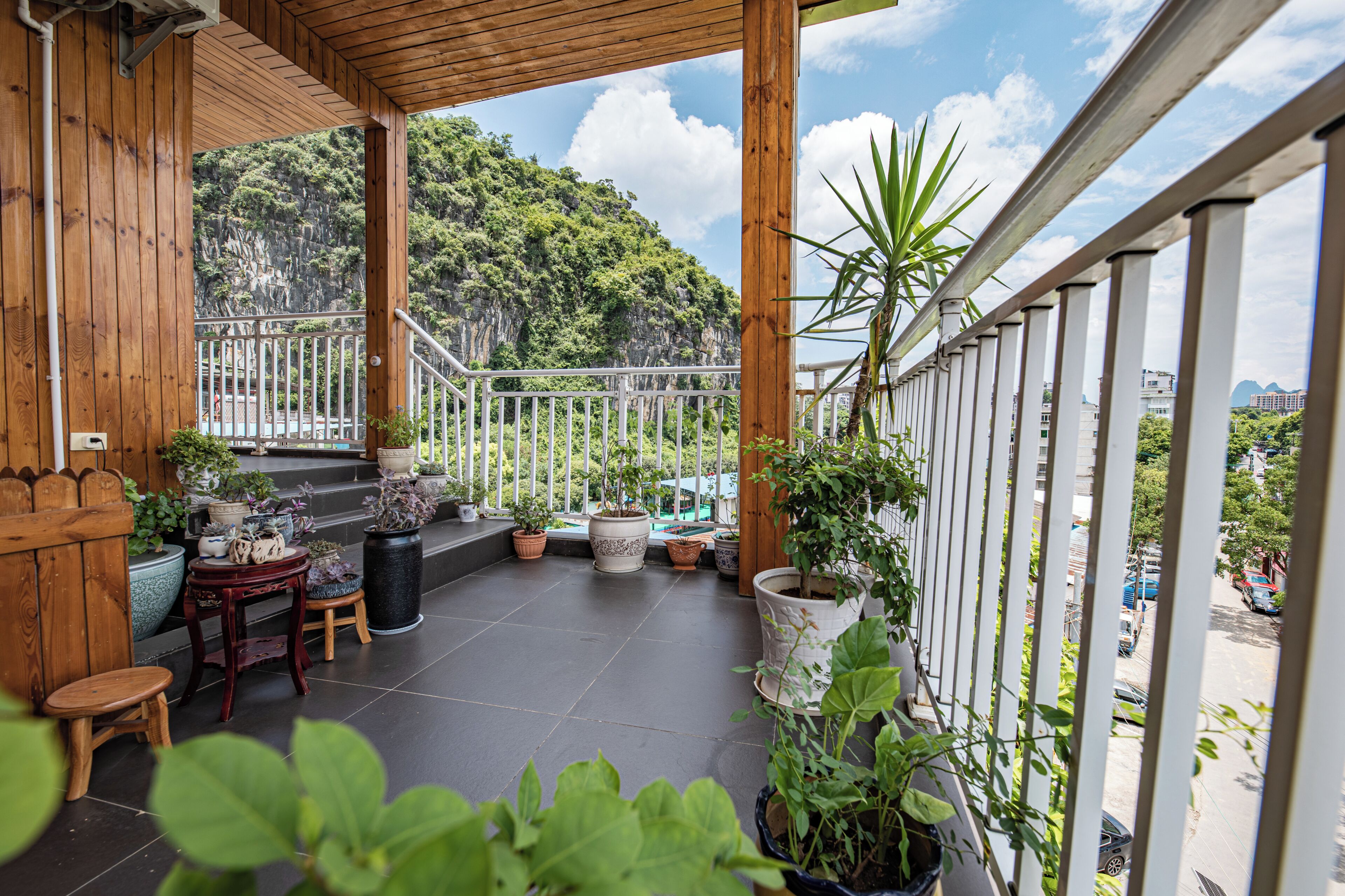 Uma varanda de madeira com plantas em vasos, uma mesa de madeira e vista para uma paisagem montanhosa.