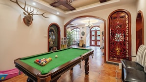 A pool table with balls, a deer head mounted on the wall, and a billiards cue rack.