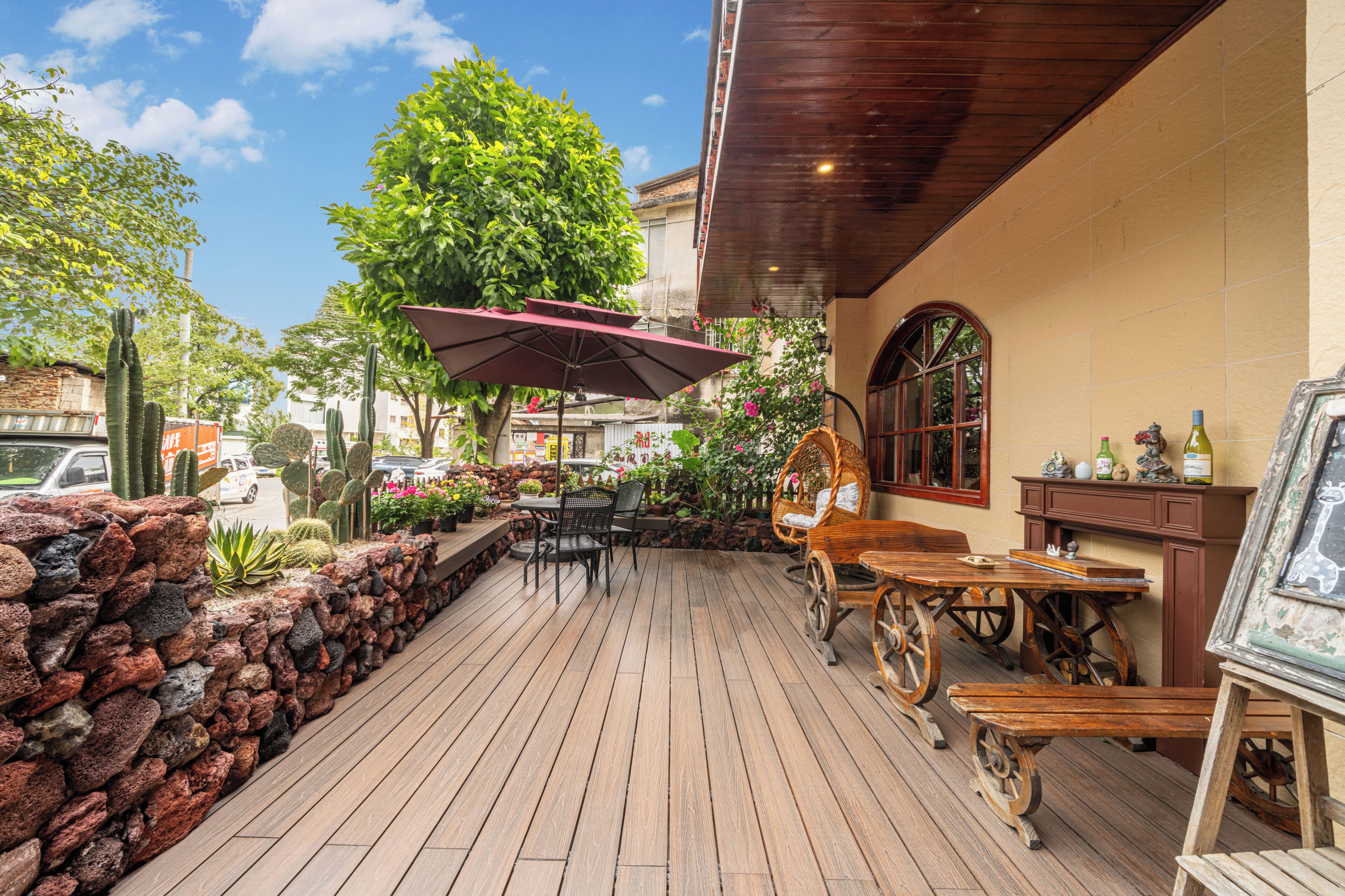 Un patio al aire libre con piso de madera, paredes de piedra y diversos arreglos de asientos, incluyendo mesas y sillas.