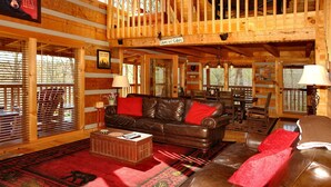A cozy cabin interior with a leather sofa, a dining area, and a loft space. - dream catcher. Beautiful Mountain Veiws and Real Log Cabin Charm! (Sevierville)