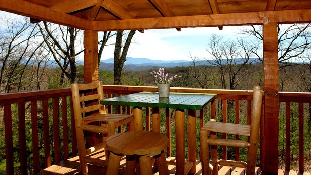 A wooden deck with a table and chairs, a potted plant, and a view of mountains. - dream catcher. Beautiful Mountain Veiws and Real Log Cabin Charm! (Sevierville)