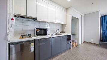 A compact kitchen with stainless steel appliances, white cabinets, and a small stool.