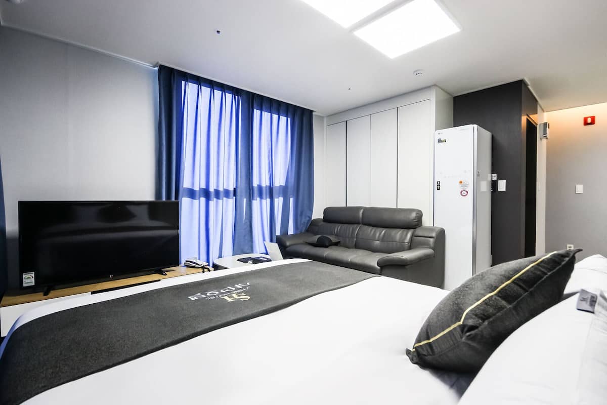A modern hotel room with a bed, a TV, a sofa, and a wardrobe.