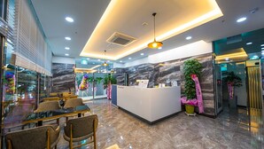 A modern hotel lobby with a reception desk, seating area, and decorative plants.