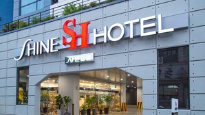 The exterior of the SHINE HOTEL with a modern design, featuring a prominent entrance and potted plants.