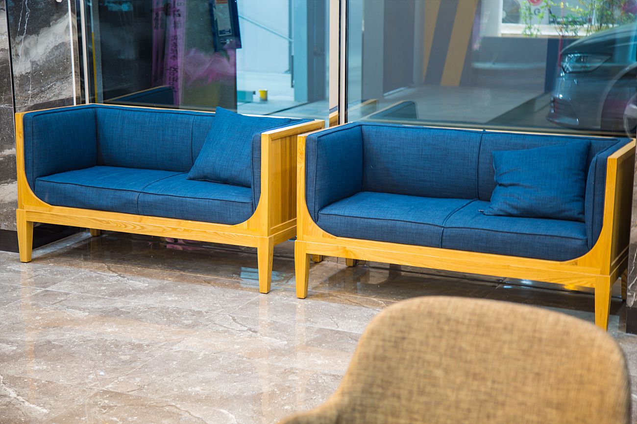 Two blue sofas with wooden frames in a modern lobby with marble flooring.