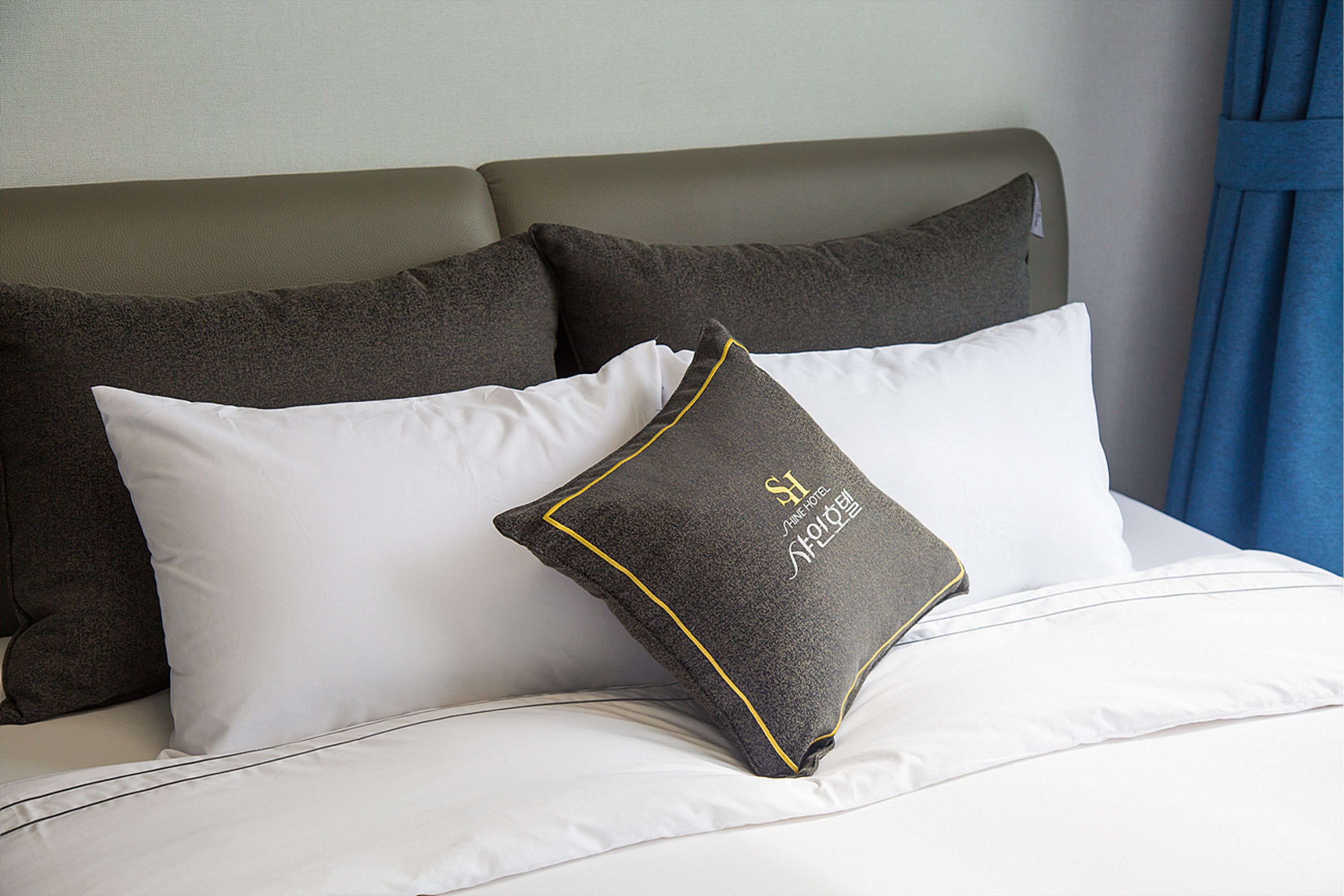 Una cama con almohadas blancas y gris oscuro, cabecera gris y cortina azul.