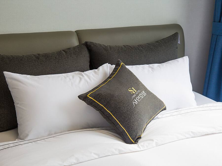 Ein Bett mit weißen und dunkelgrauen Kissen, einem grauen Kopfteil und einem blauen Vorhang.