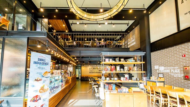 A modern cafe with a mezzanine level, wooden furniture, and a variety of seating options.