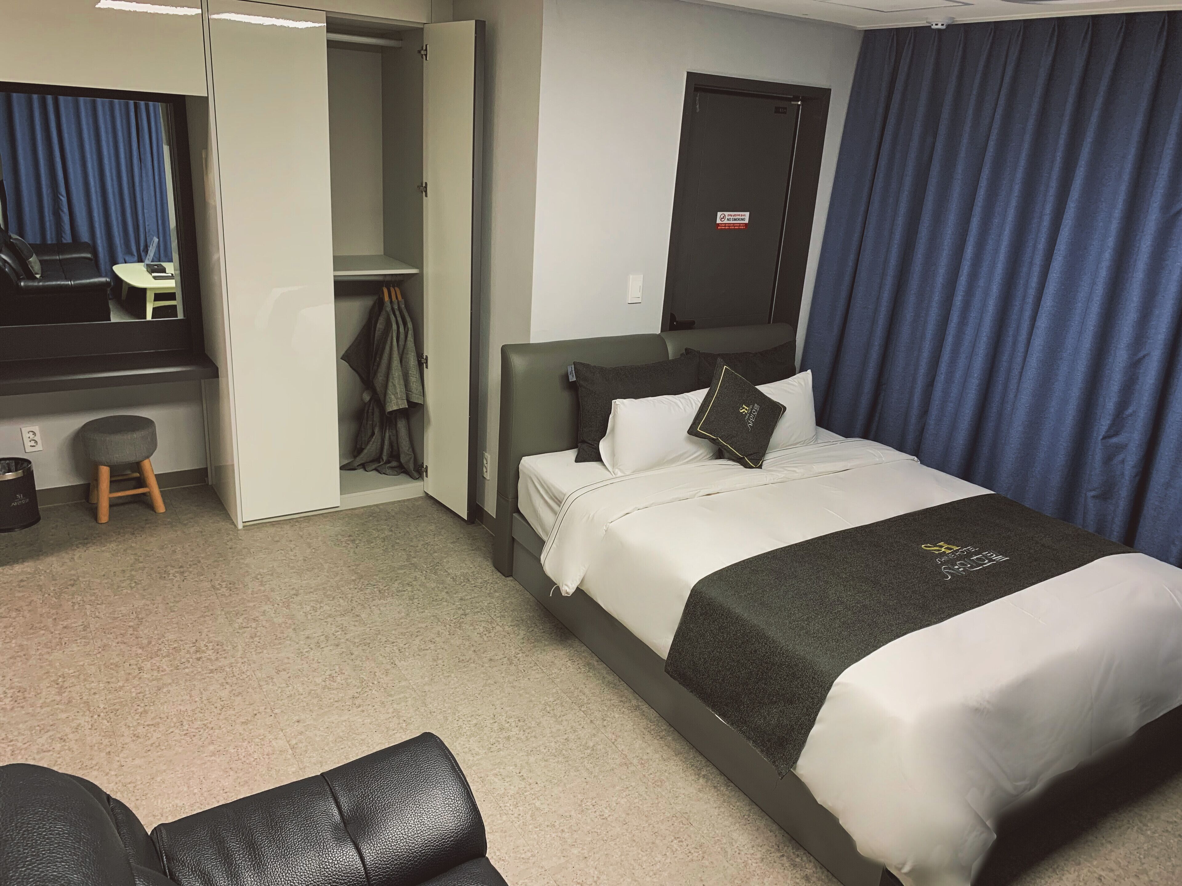 A hotel room with a bed, a desk, a chair, a wardrobe, and a mirror.