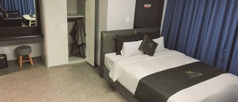 A hotel room with a bed, a desk, a chair, a wardrobe, and a mirror.