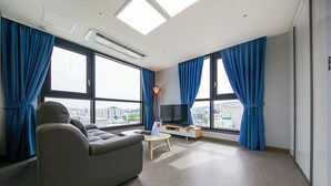 A modern hotel room with a sofa, a TV, and large windows with curtains.